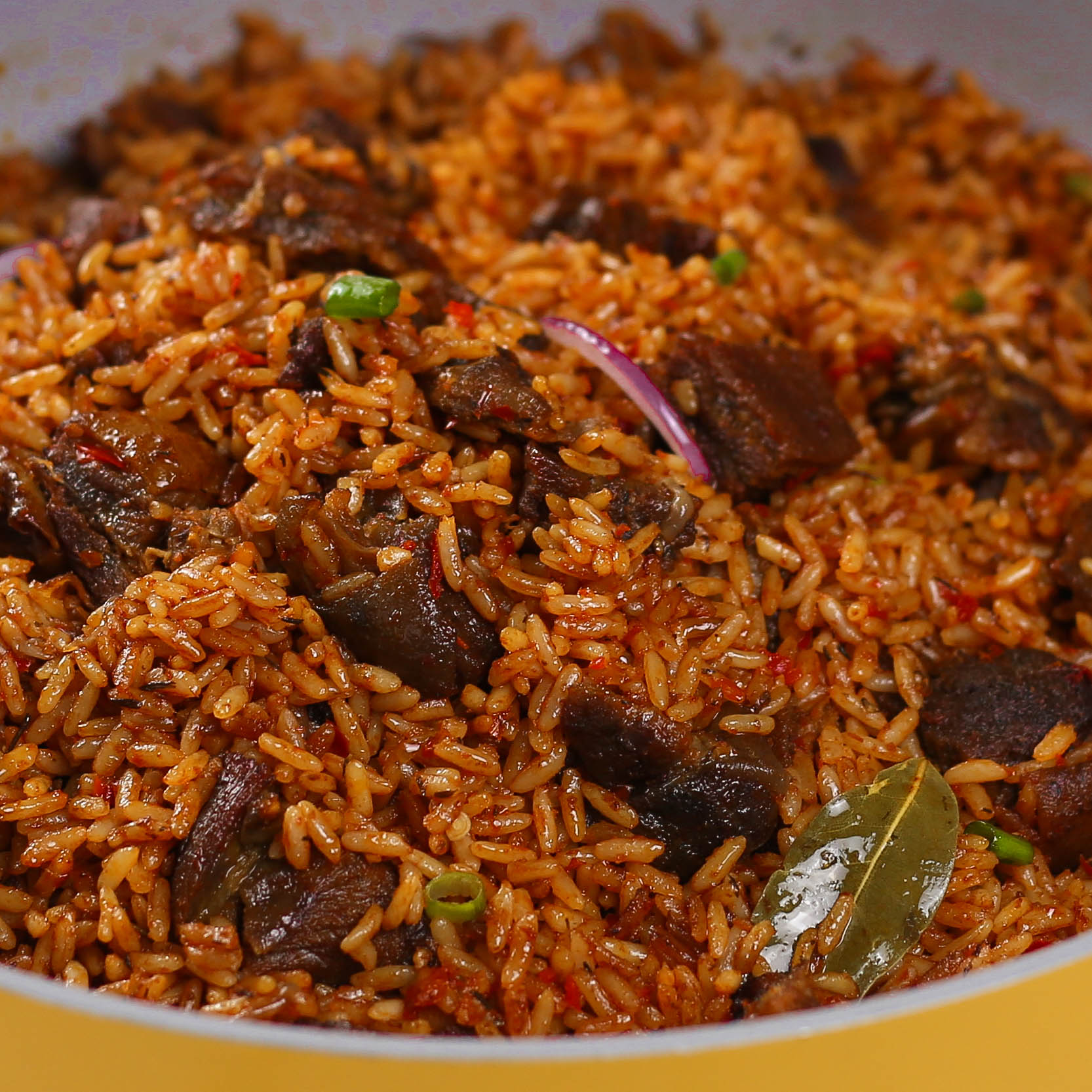 Appetizing close-up of asun jollof rice featuring vibrant red jollof rice mixed with chunks of spicy grilled goat meat (asun), topped with fresh herbs, plated in a white bowl for an inviting presentation